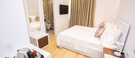 Una habitación de hotel moderna con una cama, mesita de noche y un escritorio pequeño con hervidor y vasos.