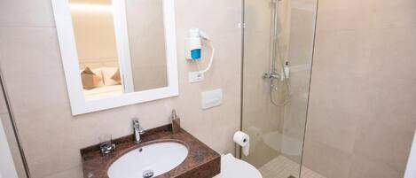 A bathroom with a marble sink, a toilet, a glass shower enclosure, and a mirror.