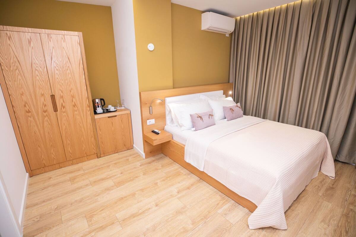 Una habitación de hotel con cama, un armario de madera, una mesita de noche con lámpara y aire acondicionado instalado en la pared.