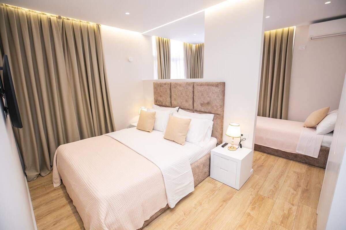 Una habitación de hotel moderna con una cama grande, una cama más pequeña, una mesita de noche con lámpara y un armario.