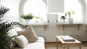 A cozy living room with a sofa, a coffee table, and two windows with plants. - Roost Pursimiehenkatu (Helsinki)