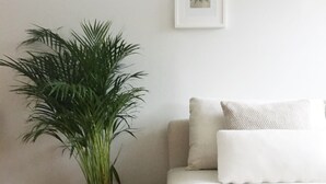 A minimalist living room with a white sofa, a large green plant in a woven pot, and a framed picture on the wall. - Roost Pursimiehenkatu (Helsinki)