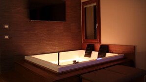 Un bagno moderno con una vasca da bagno ampia, una televisione a muro e uno specchio.