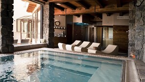Piscina interna con sedie a sdraio, pareti in pietra e travi in legno.