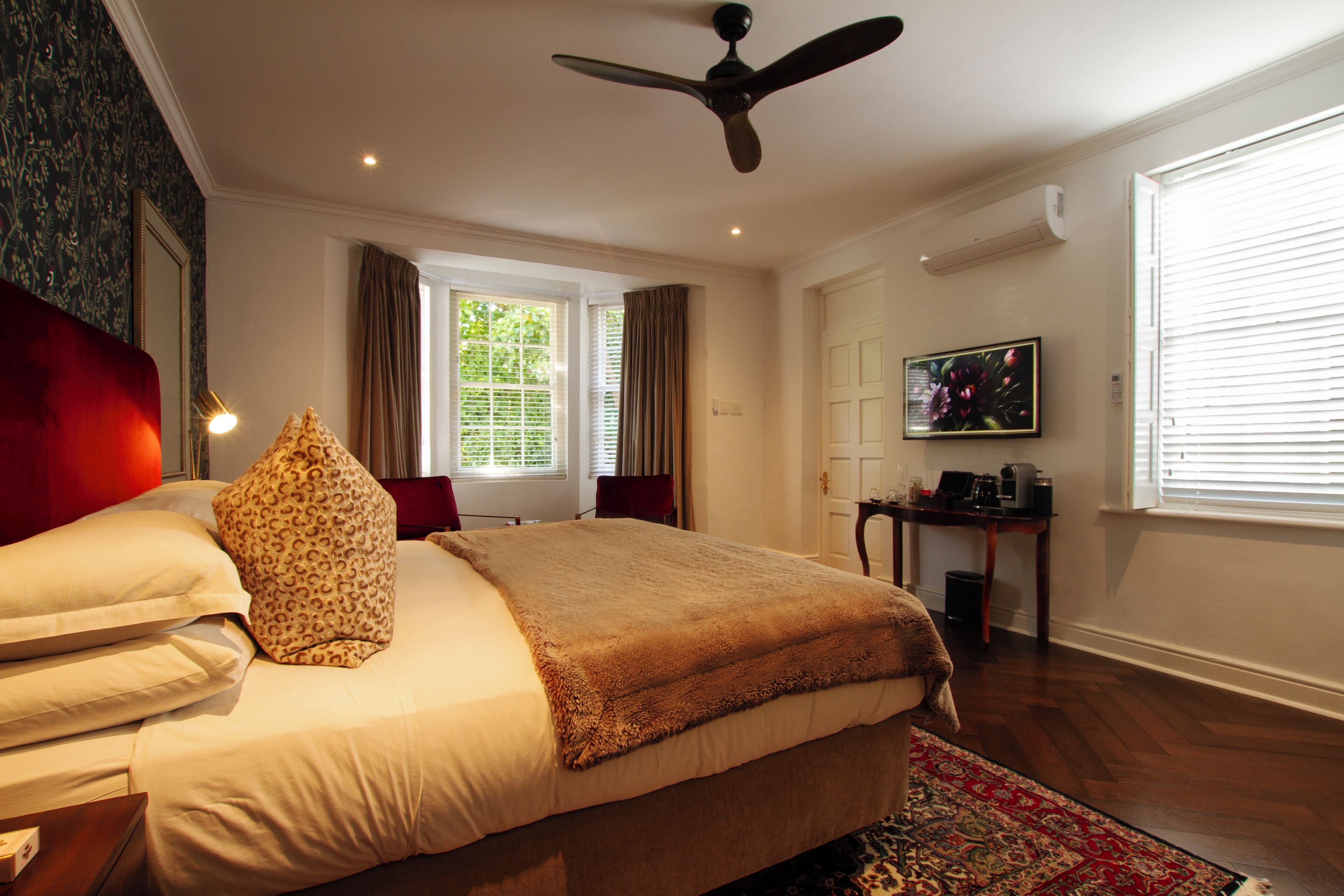 A bedroom with a bed, a ceiling fan, a window with curtains, a TV, and a desk with a chair.