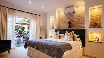 A hotel room with a large bed, a sitting area with a chair, a view of the outdoors, and a brick wall.