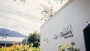 Guest house with a charming exterior, set amidst lush greenery and a mountain range.
