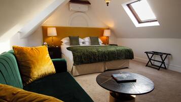 Una habitación con una cama, un sofá verde, una mesita, una lámpara y un tragaluz.