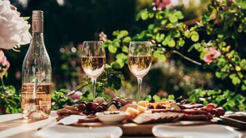 A table with a bottle of wine, two glasses, and a variety of cheeses and fruits.