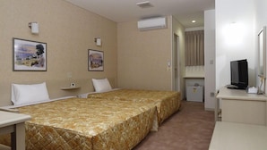 Una habitación de hotel con dos camas, un escritorio, un televisor y dos unidades de aire acondicionado fijadas a la pared.