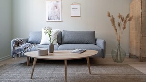 A modern living room with a grey sofa, a round wooden coffee table, and a vase with dried plants. - Roost Eerikinkatu (Helsinki)