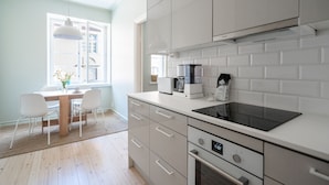 A modern kitchen with white cabinets, a built-in oven, and a coffee maker. - Roost Eerikinkatu (Helsinki)