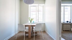 A dining area with a wooden table, four white chairs, a woven rug, and a hanging light fixture. - Roost Eerikinkatu (Helsinki)