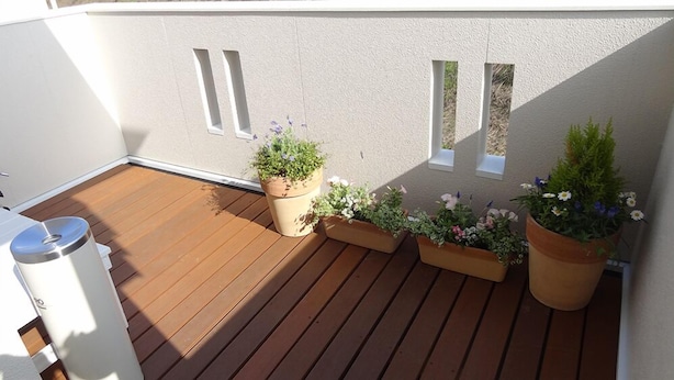 Um deck de madeira com vasos de plantas e uma lata de lixo.