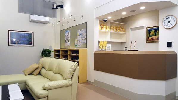 A reception area with a beige sofa, a bulletin board, a clock, and a shelf with yellow items. - Family Lodge Hatagoya Tottori Kurayoshi (Yurihama)