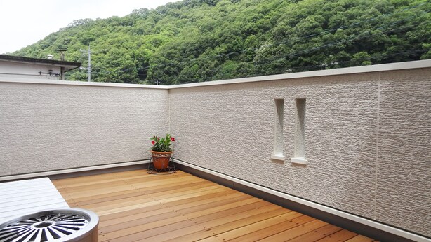 Una terraza de madera con una planta en maceta, una pequeña mesa y una pared texturizada con un ventanal.