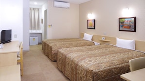 A hotel room with two beds, a desk with a computer, a small fridge, and a TV.