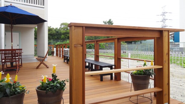 Una terraza de madera con mobiliario exterior, que incluye una mesa y sillas, y plantas en macetas.