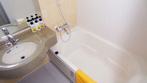 Un baño con lavamanos, espejo y bañera. Hay artículos de tocador en la encimera.