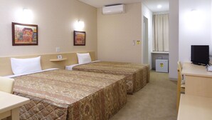 Habitación de hotel con dos camas, un escritorio, una silla, un televisor y aire acondicionado.