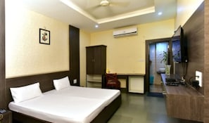 A hotel room with a bed, a desk, an air conditioning unit, and a television. - Silver Inn (Bhopal)