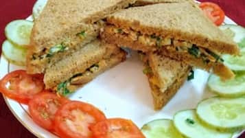 A sandwich on a plate with cucumber slices and tomato slices around it.