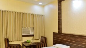 A hotel room with a bed, a small table with chairs, and a window with curtains.
