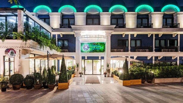 Um hotel com entrada central, várias varandas e fachada bem iluminada.