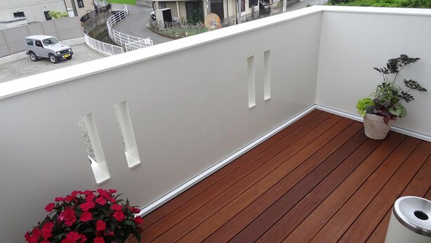 Een balkon met een houten vloer, een bloempot en een prullenbak.
