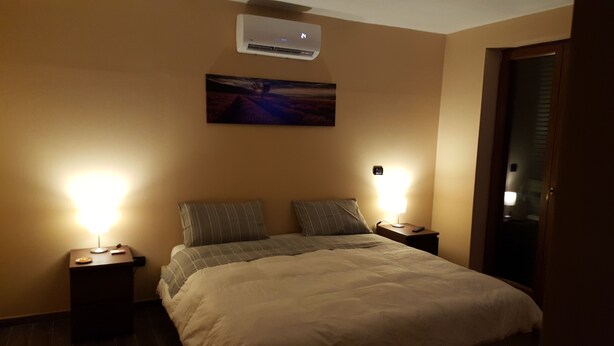 Une chambre d’hôtel comprenant un lit, deux tables de chevet, une petite table, un climatiseur fixé au mur et un tableau au-dessus du lit.