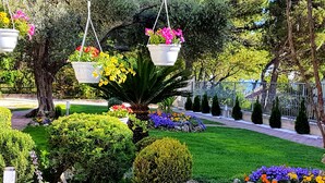Ein gepflegter Garten mit verschiedenen Blumentöpfen und Blumen, einem Kiesweg und ordentlich geschnittenen Hecken.