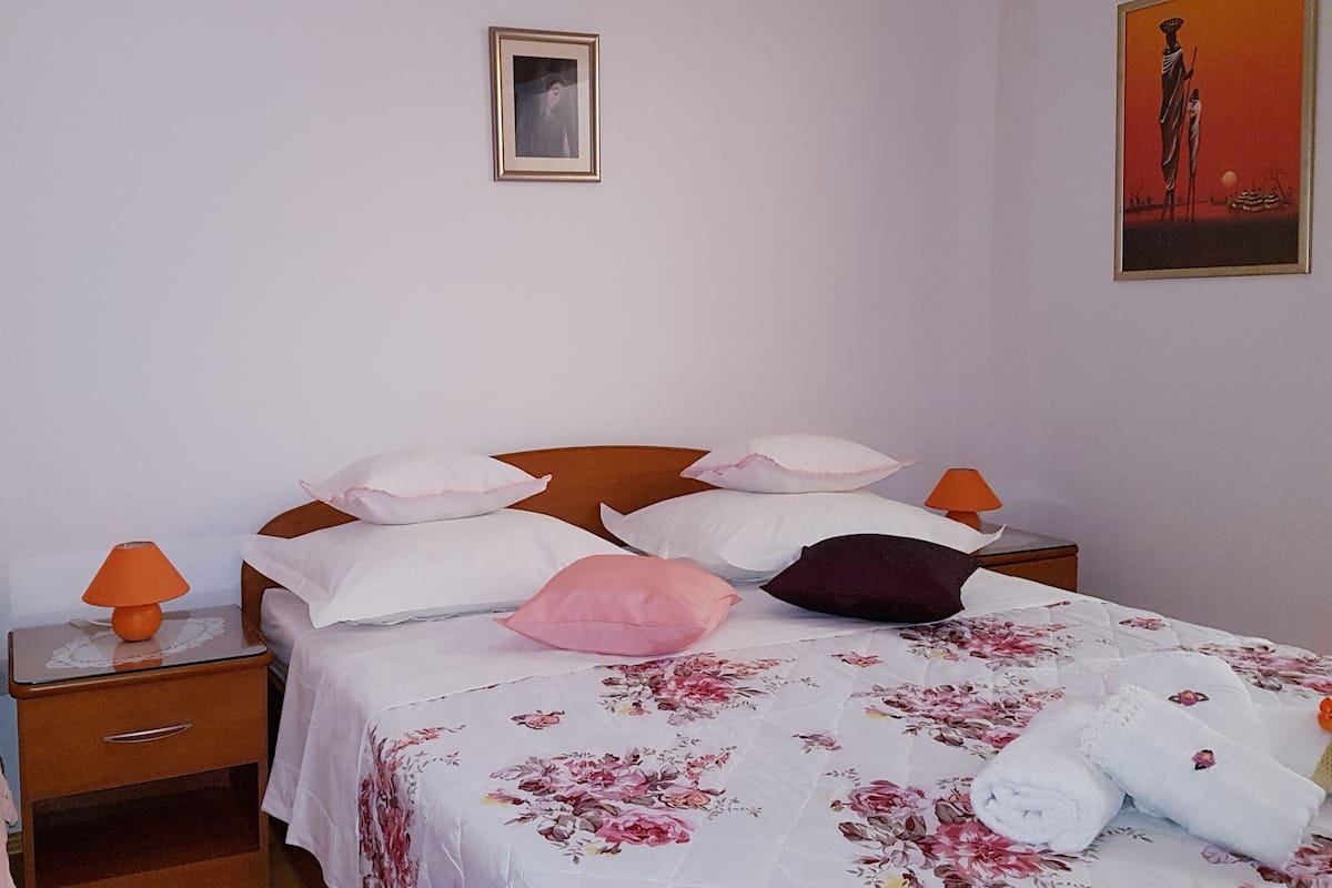 Une chambre à coucher avec un lit, des oreillers, une table de chevet, une lampe, une commode et un tableau accroché au mur.