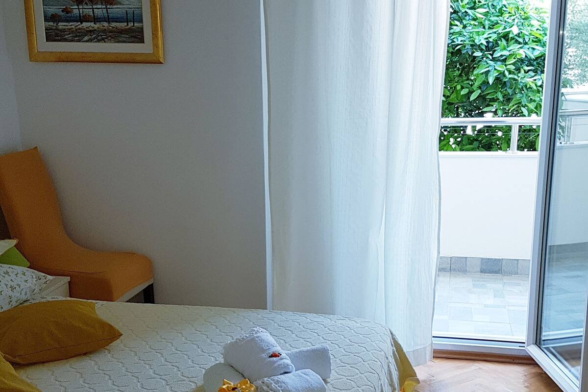 Une chambre d’hôtel avec un lit, une chaise, un tableau au mur et une vue sur la verdure par la fenêtre.
