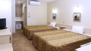 Une chambre d’hôtel avec deux lits, un bureau avec une télévision, un appareil de climatisation et une petite étagère avec une horloge.