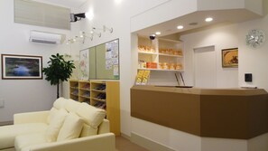 A reception area with a white sofa, a reception desk, shelves with books, a clock, and a framed picture on the wall. - Family Lodge Hatagoya Okayama (Okayama)