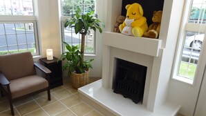 Un salon avec une cheminée, un fauteuil, une plante en pot et une étagère remplie de peluches.