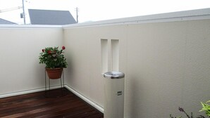 Un balcon avec un plancher en bois, une plante en pot et une poubelle cylindrique.