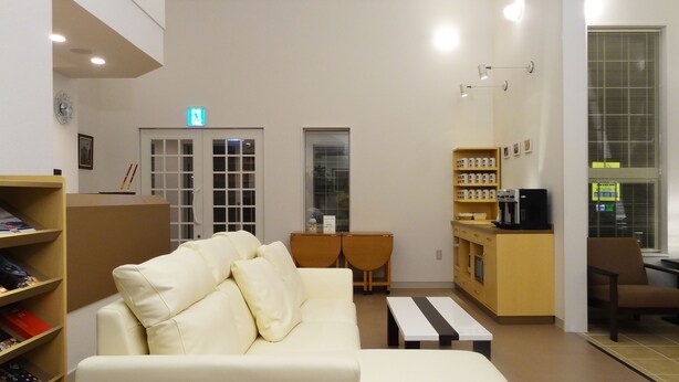 Une pièce bien éclairée, avec un canapé blanc, une petite table, une machine à café et une bibliothèque.