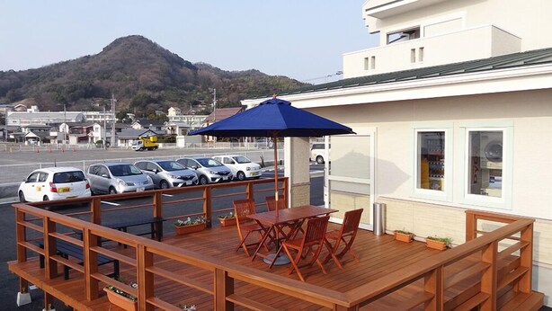 A wooden deck with a table and chairs, a blue umbrella, and a view of parked cars and a mountain in the background. - Family Lodge Hatagoya Matsuyama (Matsuyama)