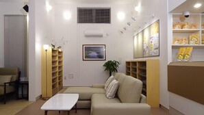 A modern waiting area with a sofa, a coffee table, a plant, and a bulletin board with information. - Family Lodge Hatagoya Matsuyama (Matsuyama)