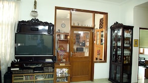 A living room with a television, wooden cabinet, and a glass display cabinet. - Dev Vatika Home Stay (Gurugram)
