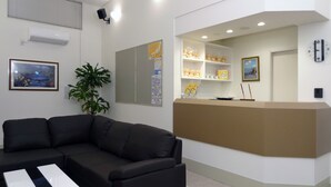 A reception area with a black sofa, a potted plant, a reception desk with shelves of teddy bears, and a clock on the wall.