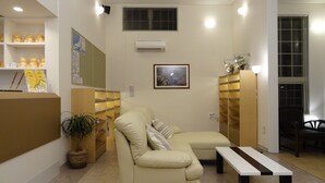 A living room with a beige sofa, a small table, a potted plant, and a wall-mounted air conditioner. - Family Lodge Hatagoya Sanuki Kanonji (Kanonji)