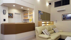 A reception area with a brown counter, a beige sofa with striped pillows, and a wall-mounted air conditioner. - Family Lodge Hatagoya Sanuki Kanonji (Kanonji)