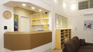 A reception area with a beige reception desk, a clock, and shelves with yellow items. - Family Lodge Hatagoya Sakaiminato (Sakaiminato)