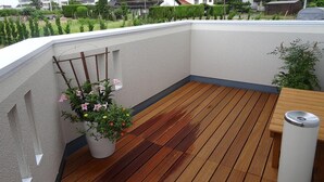 A rooftop terrace with a wooden deck, a white wall, and a potted plant with pink flowers. - Family Lodge Hatagoya Izumo Taisha (Izumo)