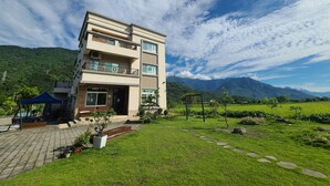 A multi-story building with a balcony, surrounded by a well-maintained lawn and a mountainous backdrop. - Flower 280 (Ji'an)