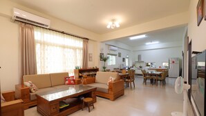 A spacious living area with a sofa, coffee table, and a dining table with chairs. There is a kitchen area in the background with a refrigerator and a microwave. - Flower 280 (Ji'an)