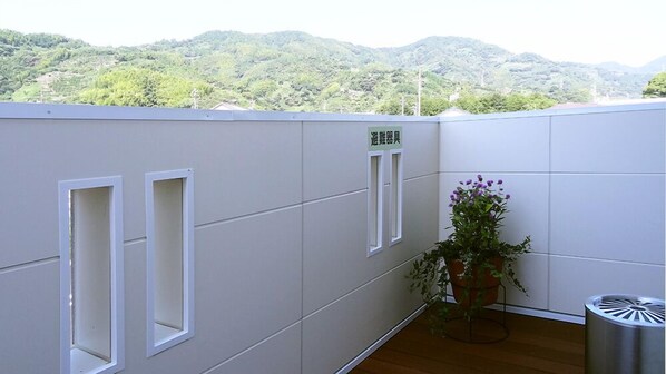 A balcony with a potted plant and a trash bin, overlooking a mountainous landscape.
