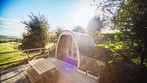 A wooden deck with a bench and a small table, leading to a covered structure with a curved roof. - Mulino Pods (Ashbourne)